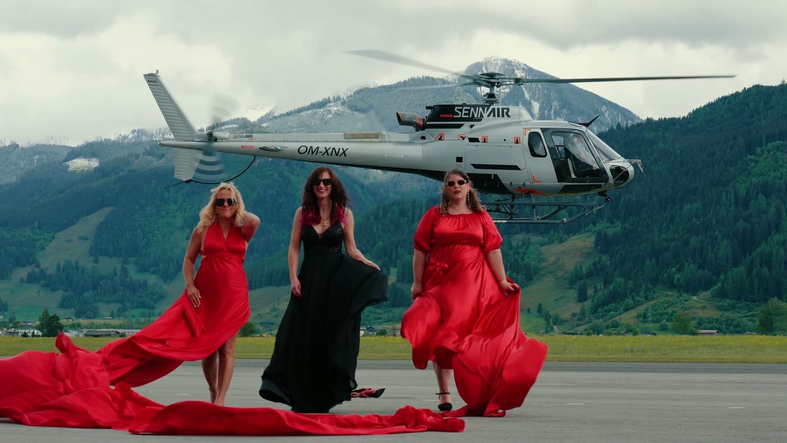 Standbild aus dem Promo-Loop: drei Frauen in Abendkleidern vor einem Helikopter